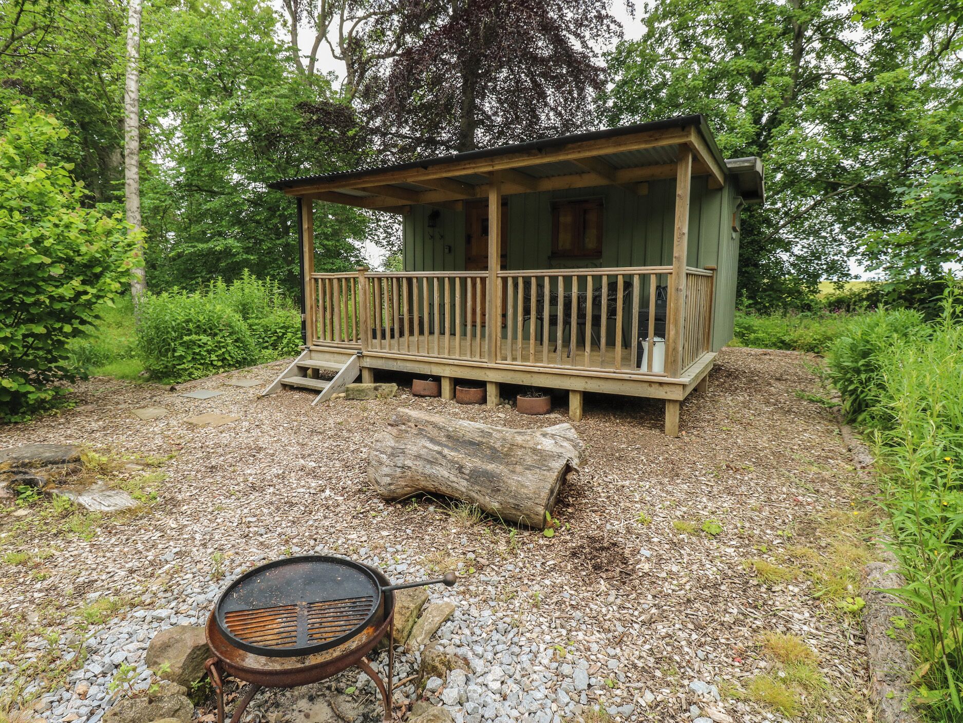 A rustic cabin with a wooden deck, a grill, and a stone pathway leading to it.
