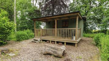 A rustic cabin with a wooden deck, a grill, and a stone pathway leading to it.