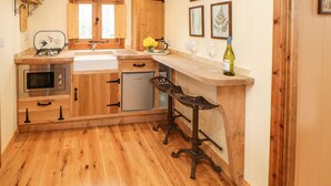 A kitchen with wooden cabinets, a built-in microwave, a sink, and a bar area with stools. - Bracken Fern (Richmond)