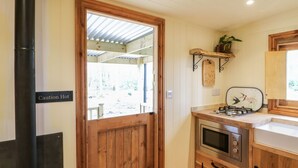 A rustic kitchen with a wood door, a stove, a sink, and a shelf with plants. - Bracken Fern (Richmond)