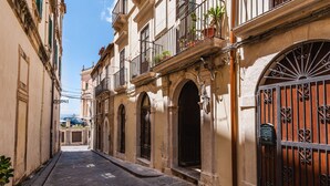 A narrow street with historic buildings, arched doorways, and a large iron gate.
