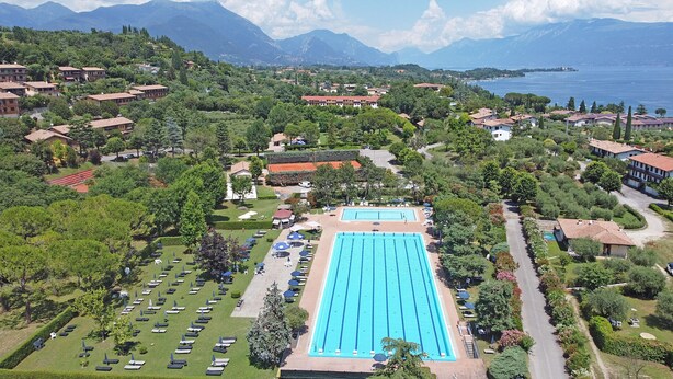 An aerial view of a resort with a large swimming pool, lush greenery, and a backdrop of mountains and a lake. - Residenza CRB 38 by Wonderful Italy (Manerba del Garda)