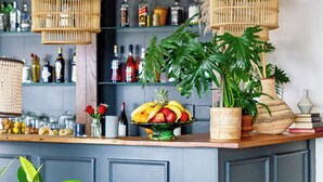 Zona de bar con lámparas de mimbre, un frutero y una variedad de botellas en estanterías.