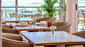 Un comedor con mesas y sillas, vista al océano y una planta en maceta.