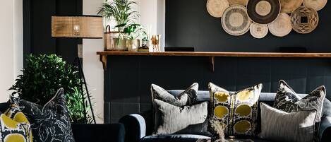 A living room with a dark-colored sofa, patterned cushions, a woven basket, and a wall-mounted tray of woven plates.