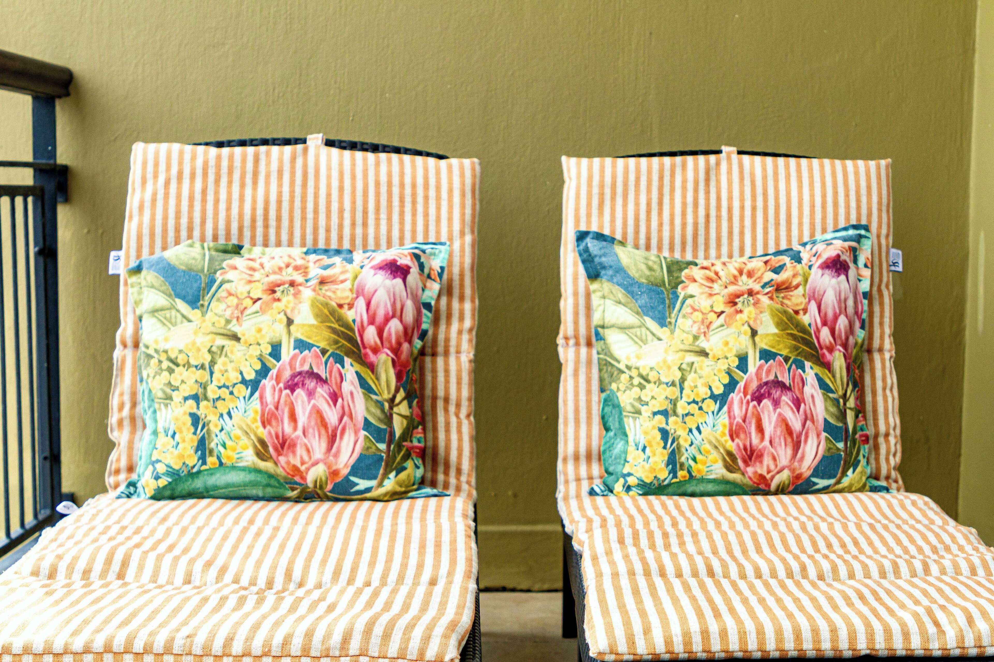 Two striped chairs with floral cushions against a plain wall.