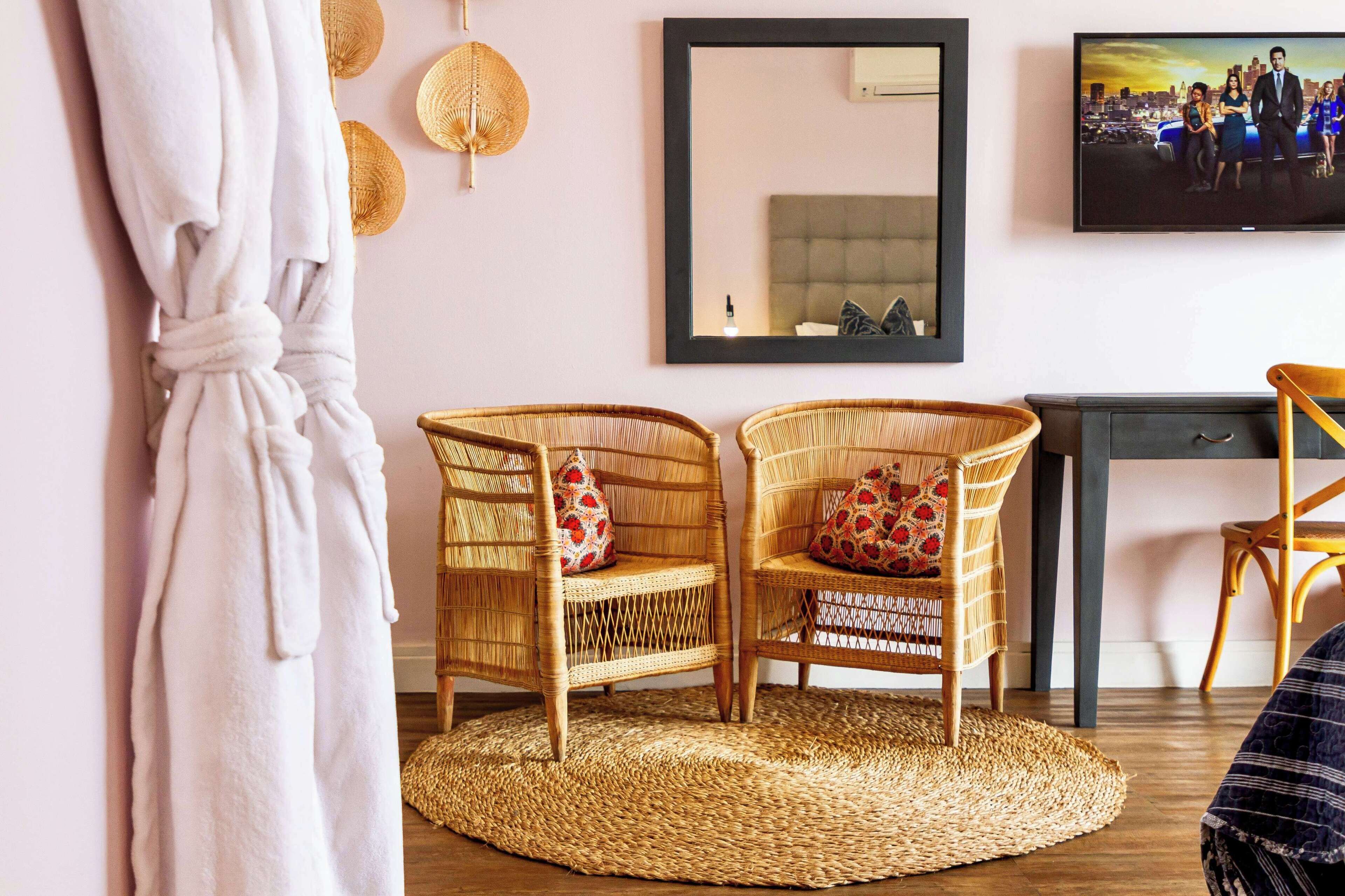 Ein Zimmer mit Korbstühlen, einem Teppich, einem Fernseher und einem Bett mit Kopfteil.