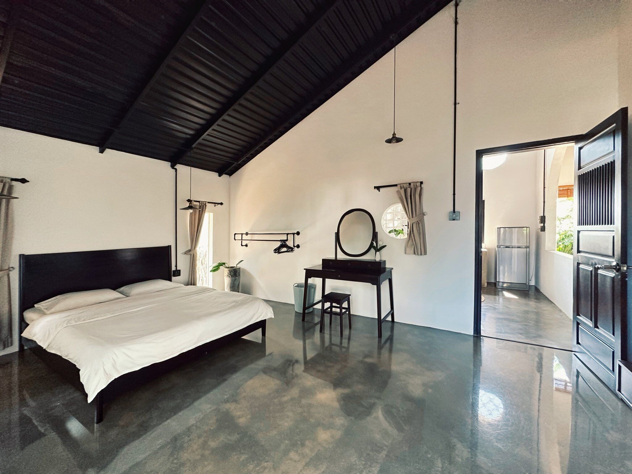 A bedroom with a bed, a desk with a mirror, and a door leading to another room.