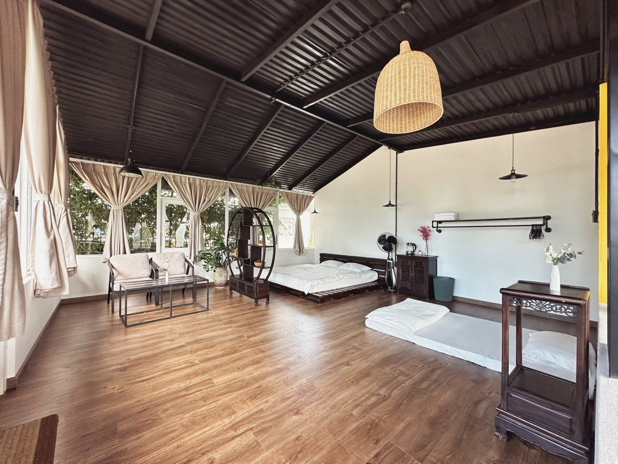 A spacious room with a large bed, a seating area with a table and chairs, a hanging light fixture, and a view of greenery outside.