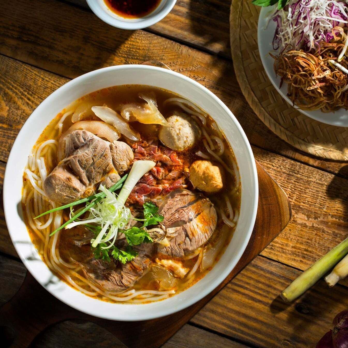 Un bol de soupe de nouilles contenant divers ingrédients, notamment de la viande et des légumes, posé sur une table en bois.