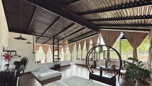 A spacious room with a large bed, a desk, and a chair. There are windows with curtains, a ceiling fan, and a potted plant. - An Nhien Farmstay & Resort (Pleiku)