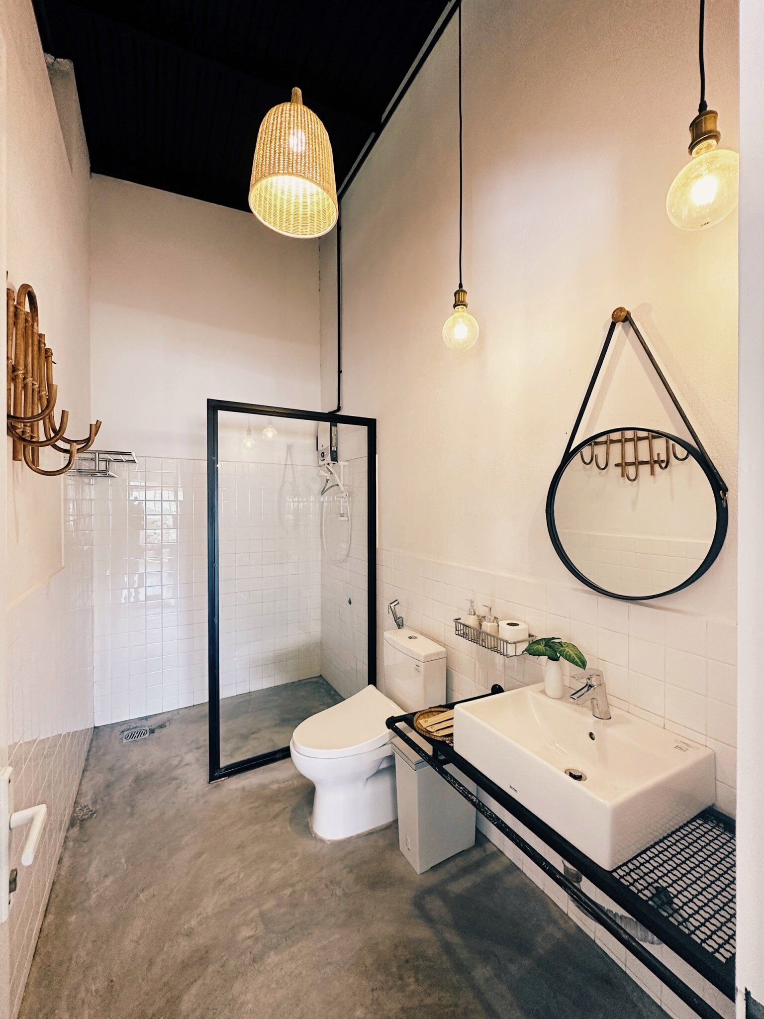 A modern bathroom with a toilet, sink, and shower. There are hanging lights and a mirror on the wall.