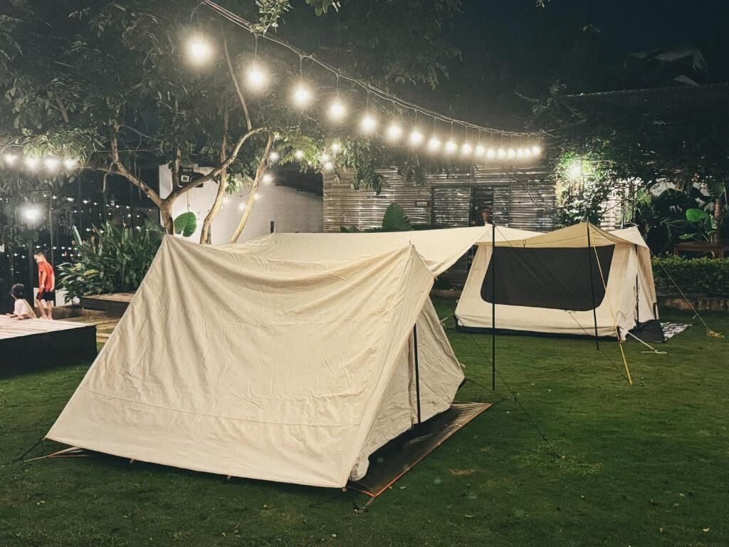 Two tents set up on a grassy area with string lights overhead.