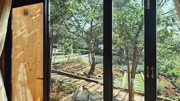 Vista desde una habitación con un ventanal grande que da a un jardín con árboles y un camino pavimentado.