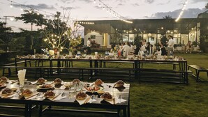 An outdoor dining area with tables set for a meal, string lights overhead, and a building in the background. - An Nhien Farmstay & Resort (Pleiku)