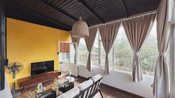 Un salón con una pared amarilla, un televisor, un sofá, una mesa de centro de vidrio y un ventilador.