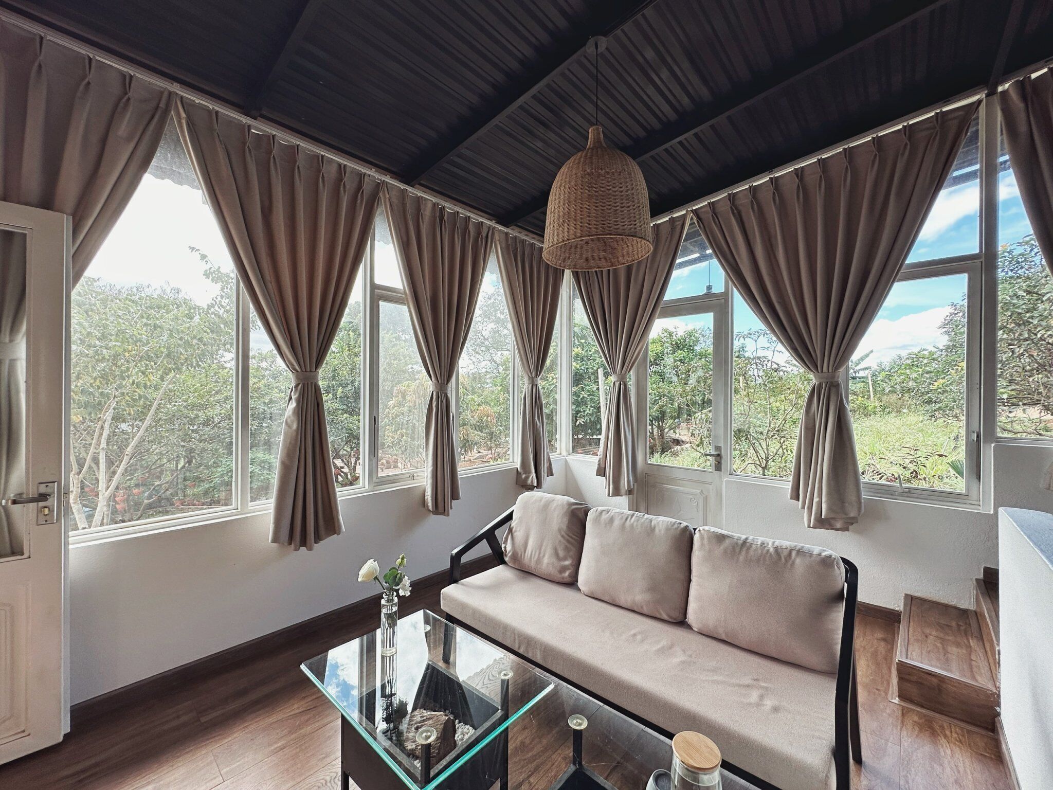 A modern living room with a sofa, a glass coffee table, and large windows with curtains.