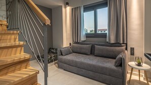 Un salon moderne avec un canapé gris, un escalier en bois et une vue sur l’extérieur grâce à une grande fenêtre.