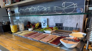 A buffet with various food items, a glass display case, and a coffee station. - Ibis Budget Muenchen Putzbrunn (Putzbrunn)