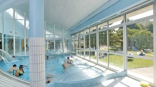 En inomhuspool med väggar av genomskinligt glas, ett kaklat golv och utsikt mot omgivningen.