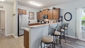 A modern kitchen with wooden cabinets, a stainless steel refrigerator, a microwave, and a bar area with stools. - Willow Bend #1411 Nice Condo! (North Myrtle Beach)