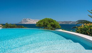 Una piscina infinita de color azul claro con vista al mar y una montaña al fondo.