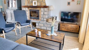 Una sala de estar con chimenea de piedra, televisor y sillones tapizados en azul.
