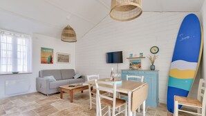 A living room with a sofa, dining table, chairs, a TV, and a surfboard.