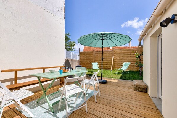 Eine Holzterrasse mit Tisch und Stühlen, einem grünen Sonnenschirm und einem kleinen Gartenbereich.