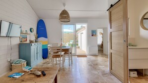 A modern kitchen with a dining area, a large surfboard, and a sliding door leading to a patio.