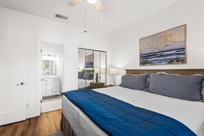 A bedroom with a bed, a nightstand, a lamp, a painting, a door, and a mirror.