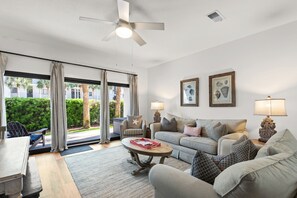 A living room with a sofa, armchairs, a coffee table, a ceiling fan, and a view through large glass doors.