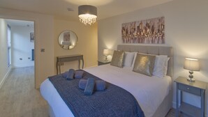 A bedroom with a large bed, two bedside tables, a chandelier, a mirror, and a cityscape painting on the wall. - Marina Walk, New Luxury Coastal Apartment in The English Riviera (Torquay)
