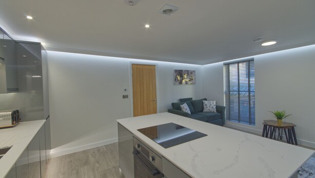 A modern kitchen with a large island, a built-in oven, and a dining area with a table and chairs. - Marina Walk, New Luxury Coastal Apartment in The English Riviera (Torquay)