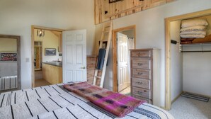 A bedroom with a bed, a dresser, a ladder, and a closet with hanging bags. - Riverfront Access | Pet Friendly | Expansive Deck w/Mtn Views | ATV's Welcome (Creede)