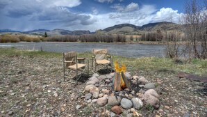 A campsite with two chairs and a campfire, surrounded by a rocky landscape and a river. - Riverfront Access | Pet Friendly | Expansive Deck w/Mtn Views | ATV's Welcome (Creede)