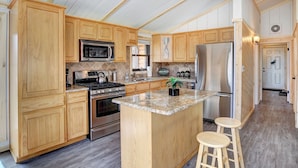 A kitchen with wooden cabinets, a stainless steel refrigerator, a microwave, a stove, and a granite countertop.