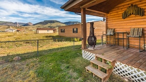 A wooden cabin with a porch, a large chimney, and a view of the surrounding landscape.
