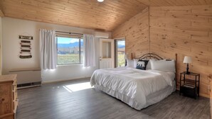 A bedroom with a wooden ceiling, a bed with white bedding, a nightstand with a lamp, and a window with curtains.