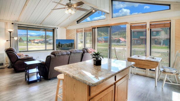 A spacious living area with a large window, a ceiling fan, and a cozy seating arrangement.