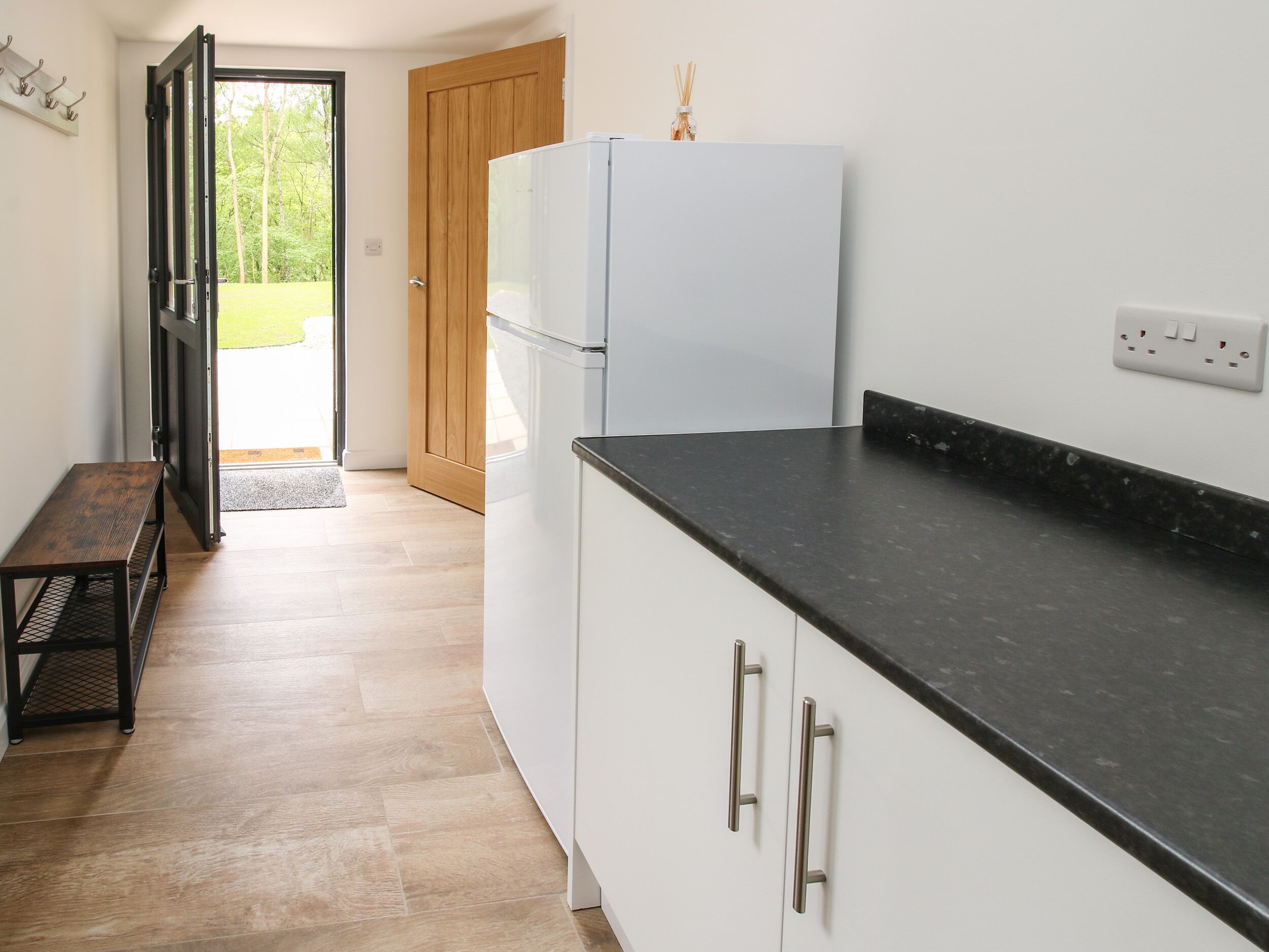 A kitchen with a white refrigerator, a black countertop, and wooden flooring.