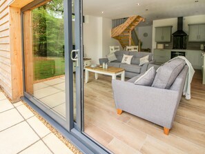 Un espacio habitable moderno con un ventanal corredero que da a un patio, un sofá gris, una mesa de centro de madera y una escalera que conecta con un nivel superior.