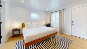 Un dormitorio moderno con una cama grande, una mesita de noche, un escritorio y una ventana con cortinas.