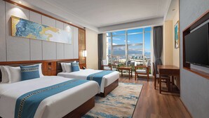Une chambre d’hôtel avec deux lits, une grande fenêtre donnant sur la ville, un téléviseur à écran plat et un coin repas.