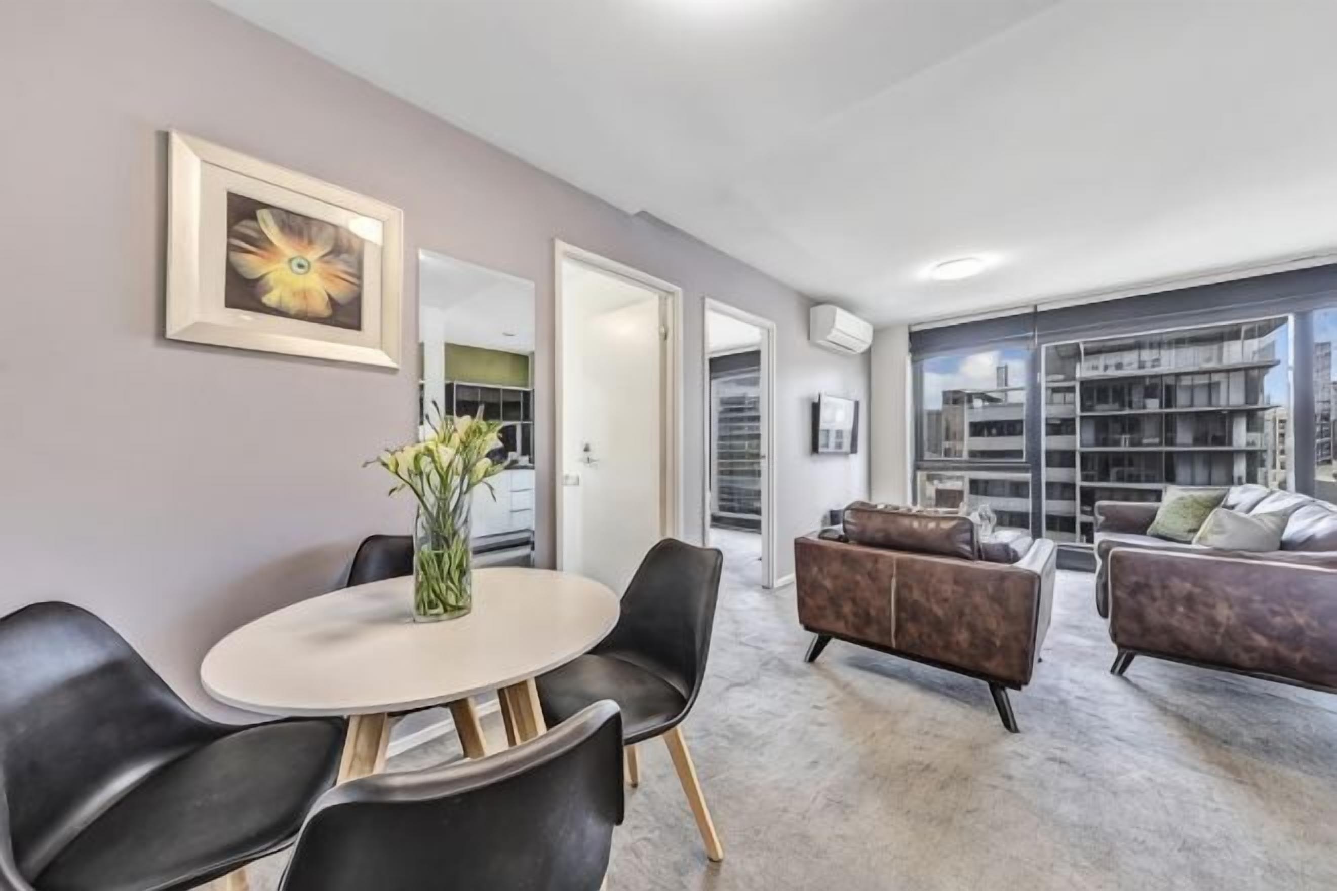 A modern living room with a round table, black chairs, a sofa, and a bookshelf.