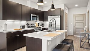 Une cuisine moderne avec des meubles de couleur sombre, des appareils en acier inoxydable et des luminaires suspendus.