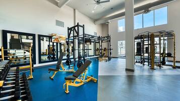 Et rummeligt fitnessrum med styrkeløftudstyr, spejle og store vinduer.