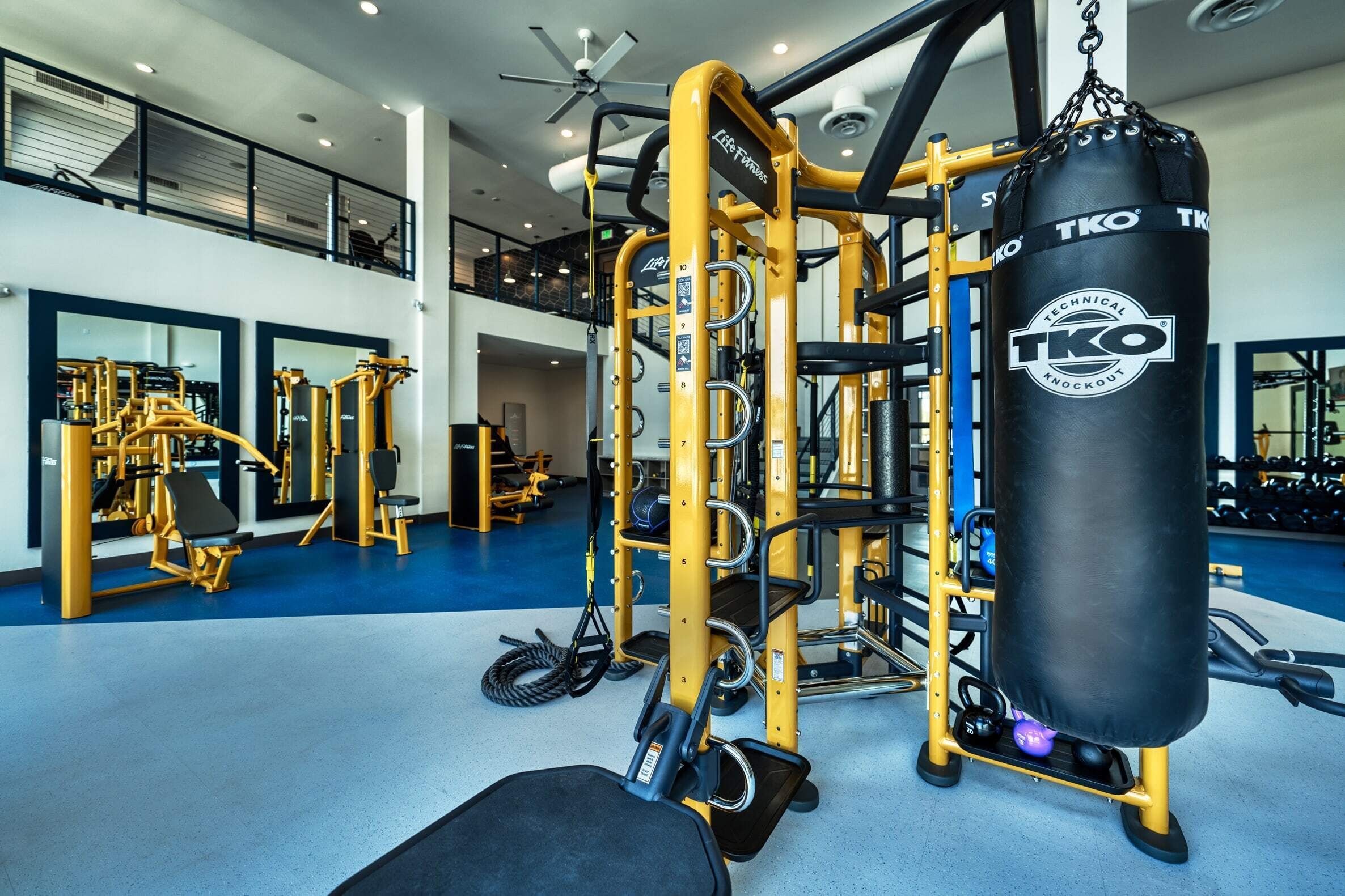 A gym with yellow equipment, a punching bag, and a ceiling fan.