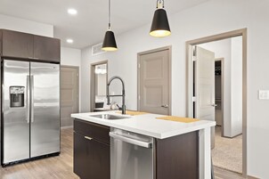 A modern kitchen with a stainless steel refrigerator, a built-in dishwasher, and pendant lighting.
