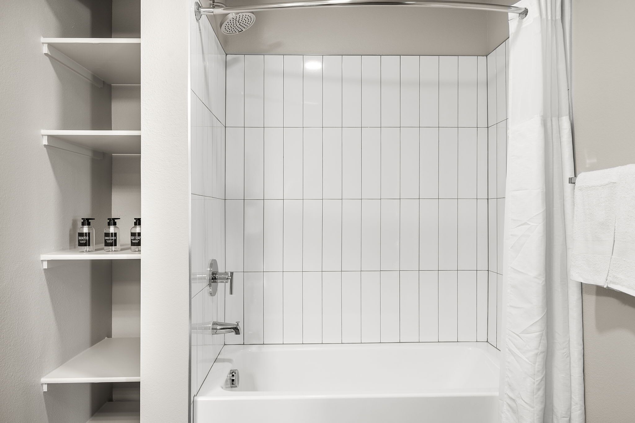 Een moderne badkamer met een bad, een douche en een plank met toiletartikelen.